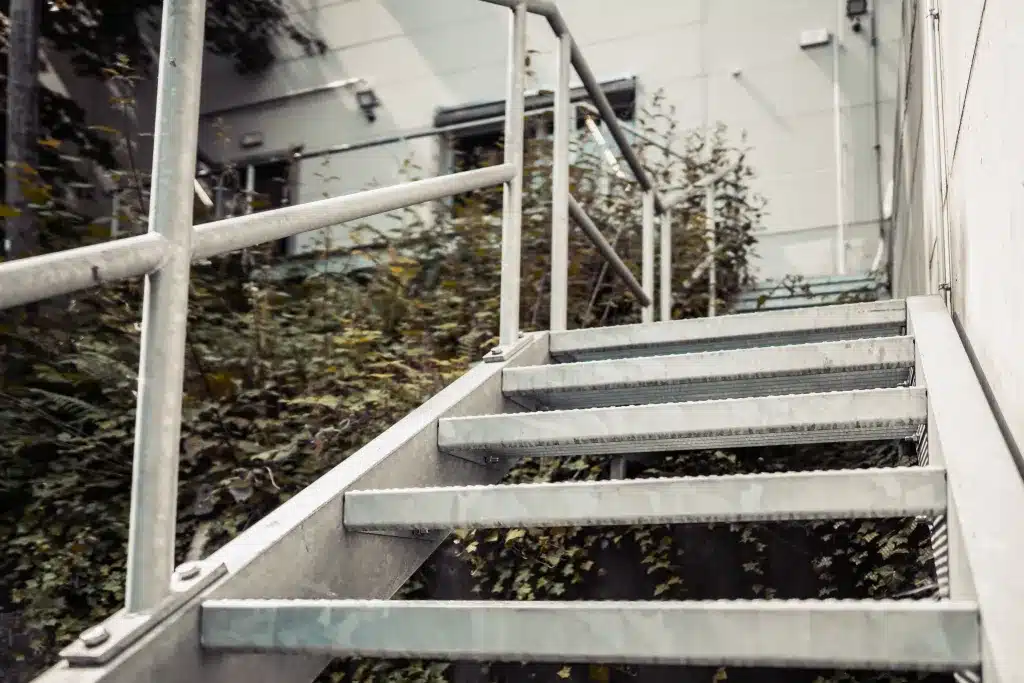 Eine Stahltreppe die von unten nach oben fotografiert ist. Die Treppe ist außen an einem Gebäude angebracht. Laufsteg aus Stahl