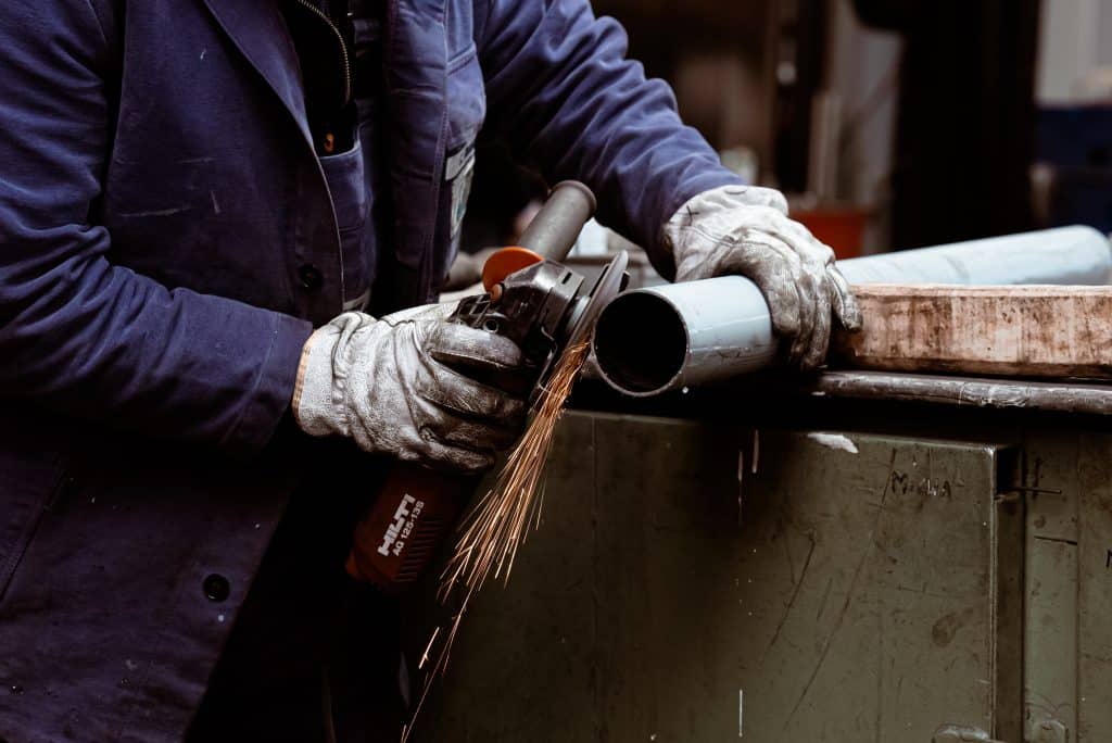 Ein Mann schleift das Ende eines Stahlrohrs mit einem handgehaltenen Winkelschleifer